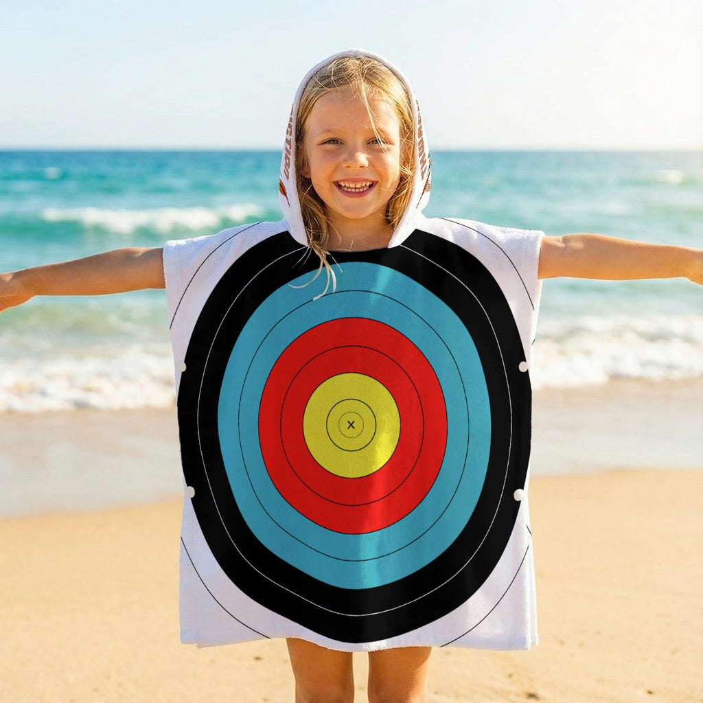 Child on a beach wearing the TLAA Target Kids' Towel Poncho, hood up, full 10-ring target face across the front