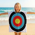 Child on a beach wearing the TLAA Target Kids' Towel Poncho, hood up, full 10-ring target face across the front