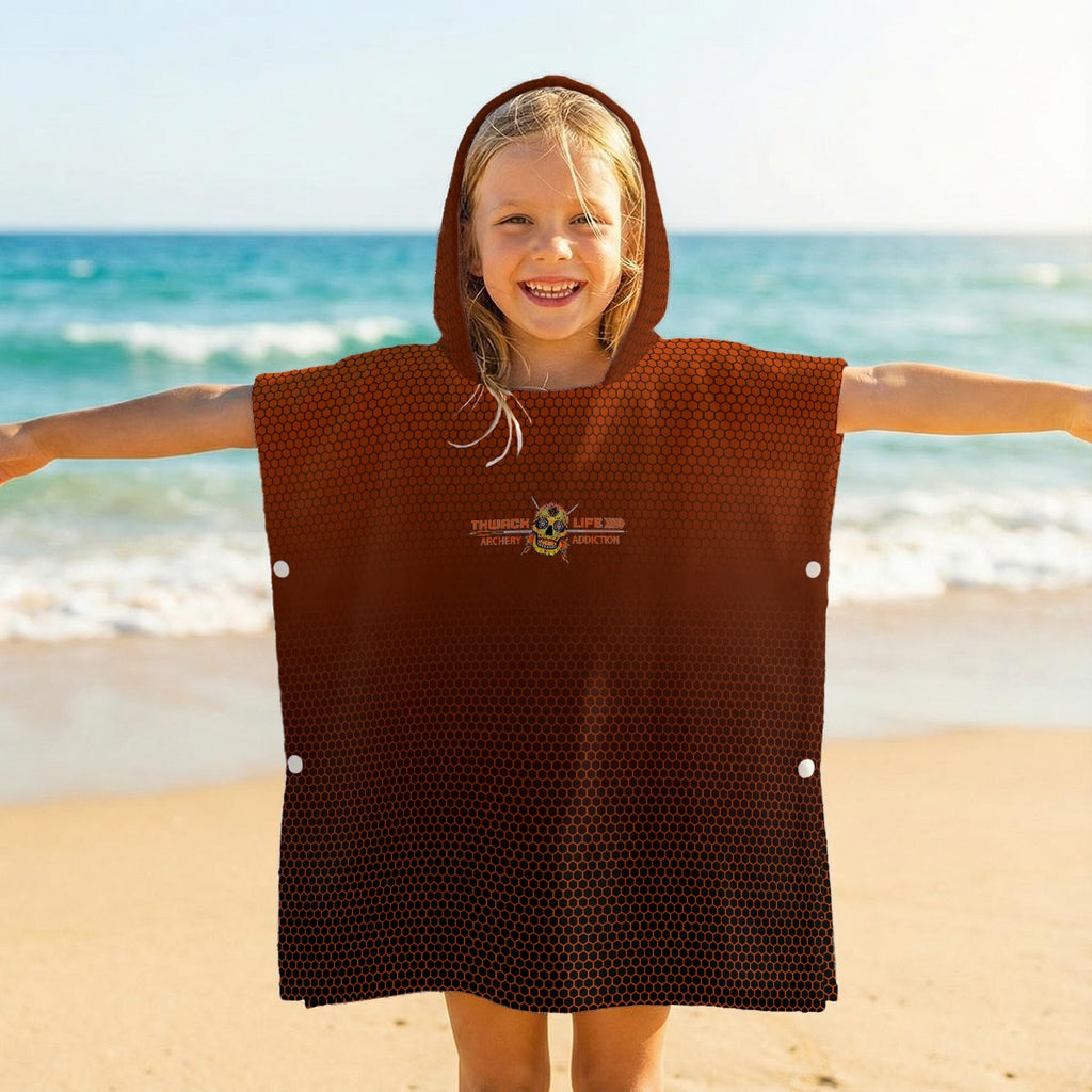 Child on a beach wearing the TLAA Sugar Skull Kids' Towel Poncho, hood up, wordmark across the front