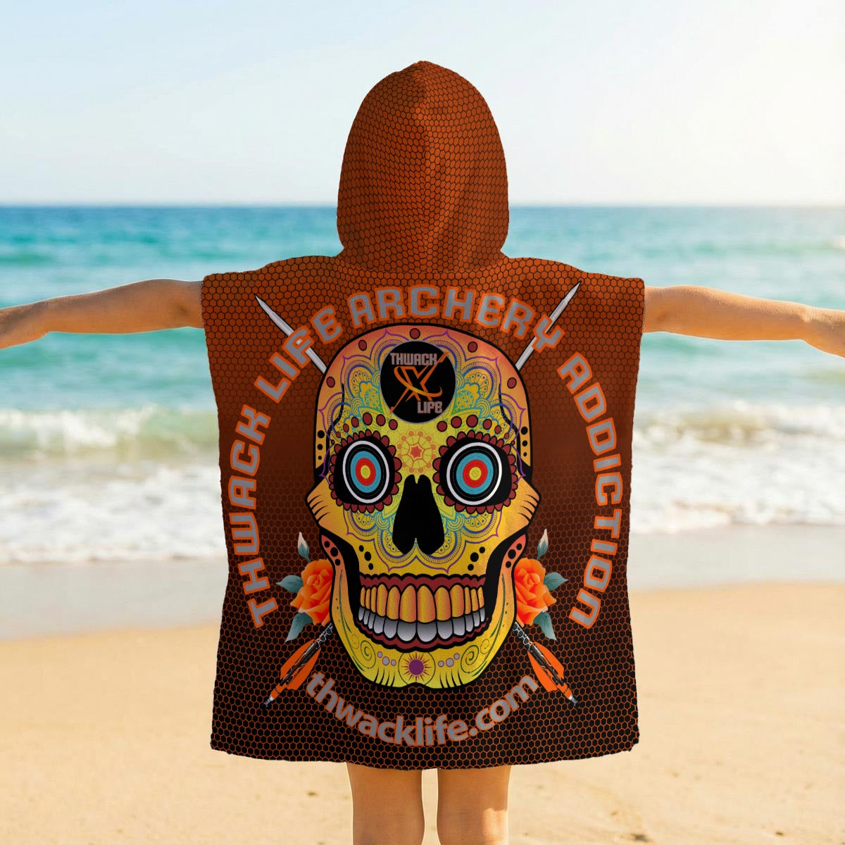 Back of the TLAA Sugar Skull Kids' Towel Poncho worn by a child, showing the full Sugar Skull medallion and Thwack Life Archery Addiction lettering