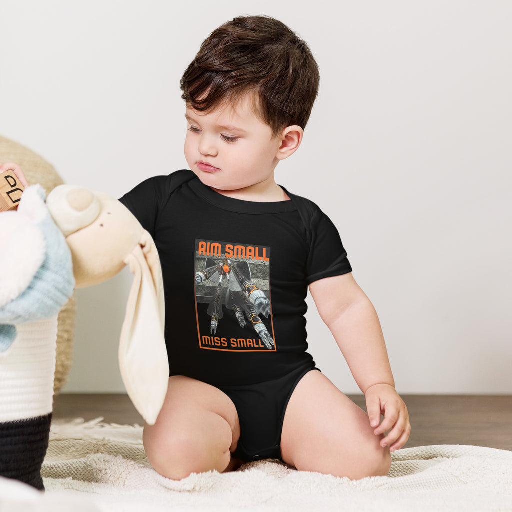 Aim Small Miss Small Baby Onesie in Black, worn by a baby sitting with a plush toy