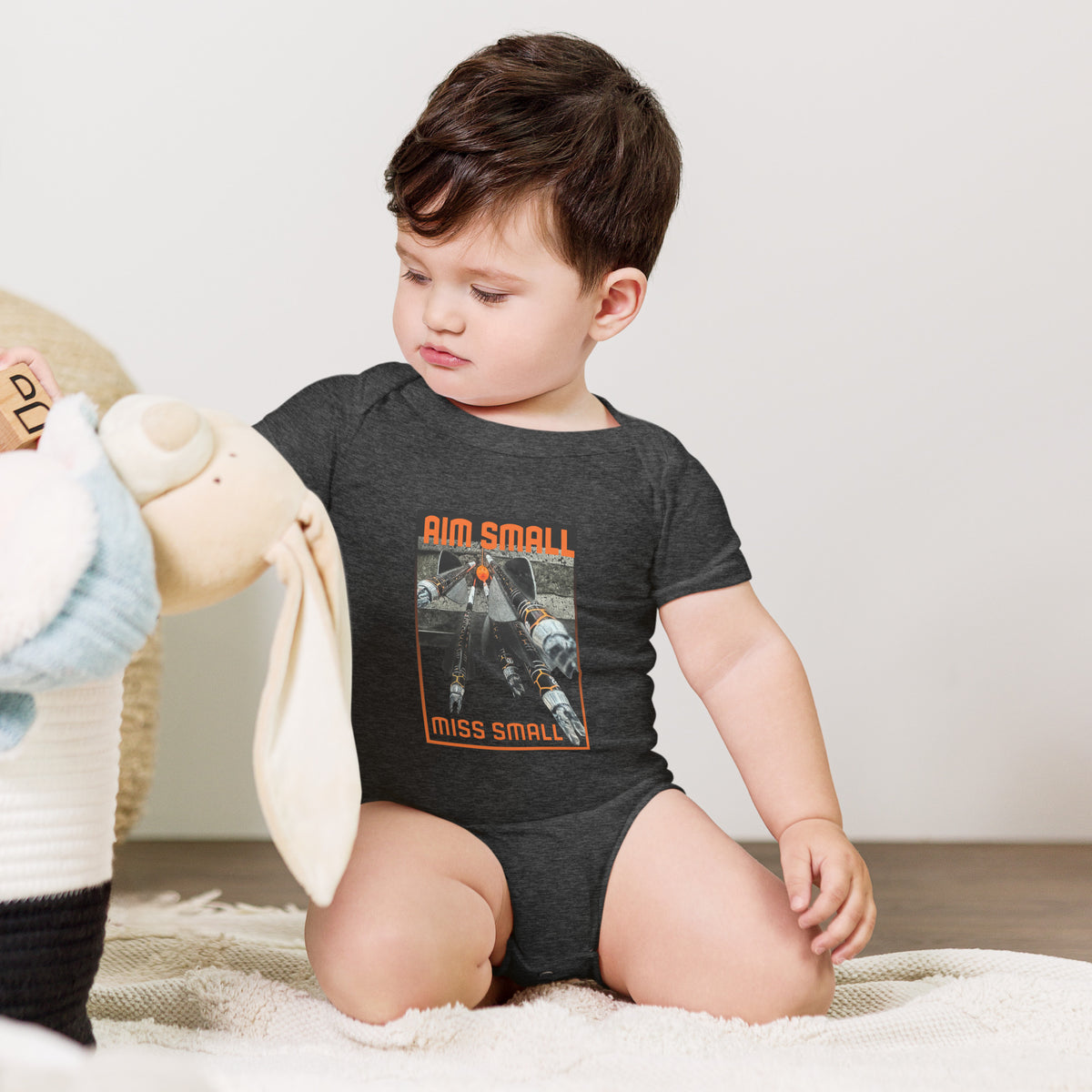 Aim Small Miss Small Baby Onesie in Dark Grey Heather, worn by a baby sitting with a plush toy