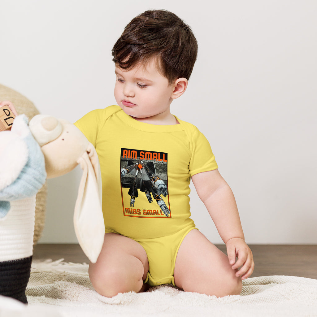 Aim Small Miss Small Baby Onesie in Yellow, worn by a baby sitting with a plush toy