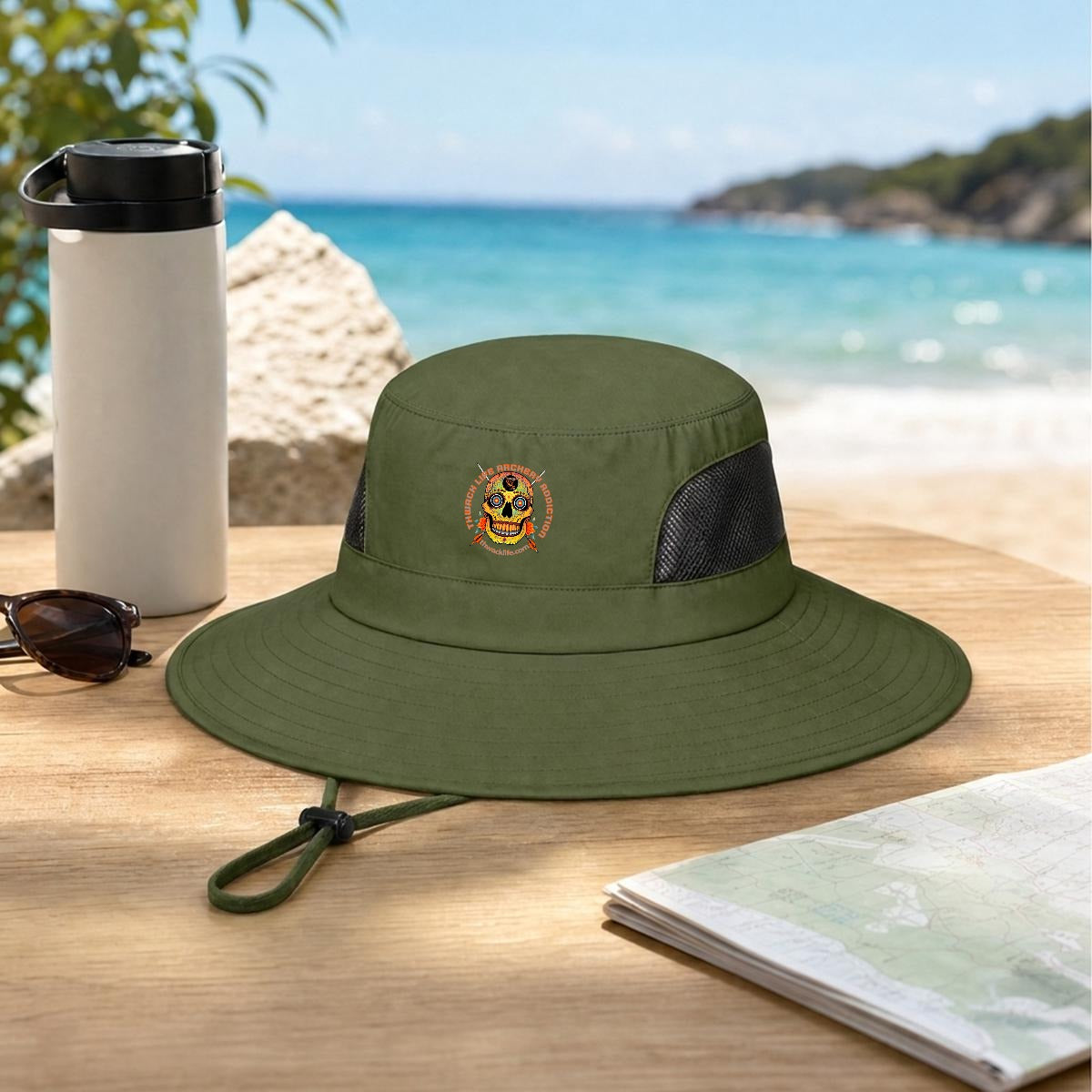 Sugar Skull Wide Brim Sun Hat in Army Green, on a table by the beach
